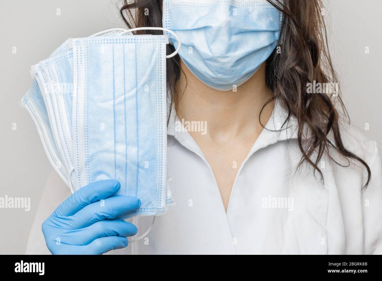 Arrestare SARSCoV, virus 2020, COVID-19. Le mani di Womans nei guanti medici blu che tengono una maschera protettiva. Medico che indossa la maschera facciale di protezione contro Foto Stock