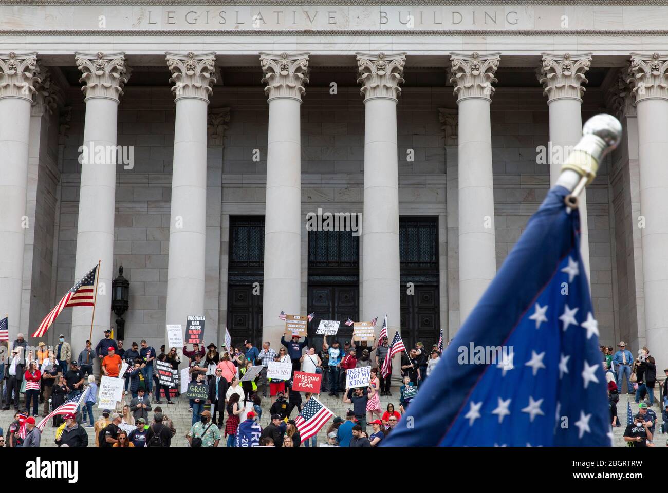 Le bandiere americane sono viste di fronte a persone che hanno segni di protesta contro le restrizioni di soggiorno a casa durante la pandemia COVID-19 sui passi di t Foto Stock