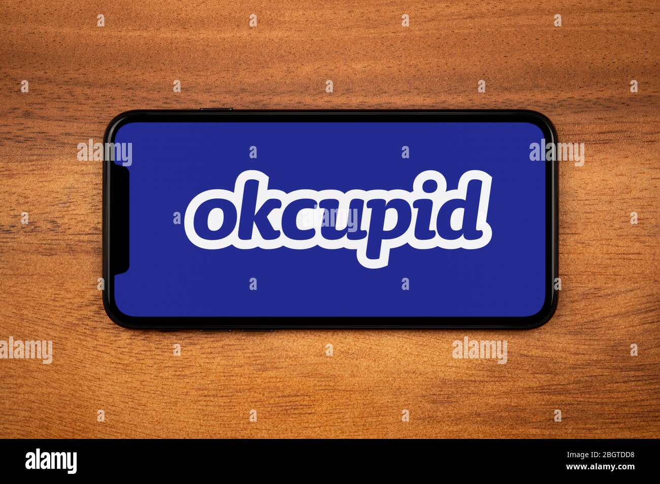 Uno smartphone con il logo okcupid è appoggiato su un tavolo di legno (solo per uso editoriale). Foto Stock