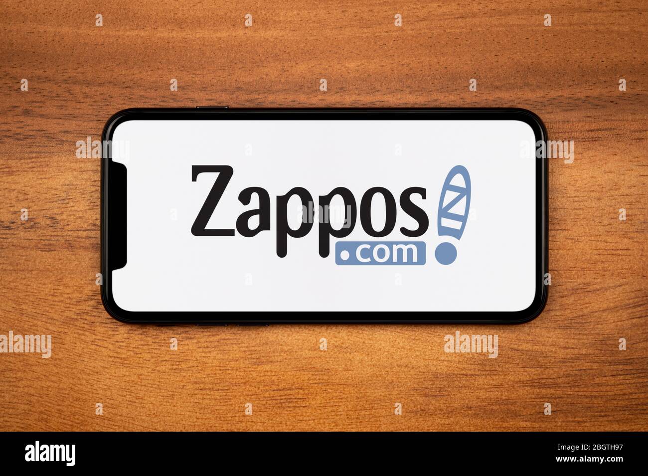 Uno smartphone con il logo Zappos si appoggia su un tavolo di legno (solo per uso editoriale). Foto Stock