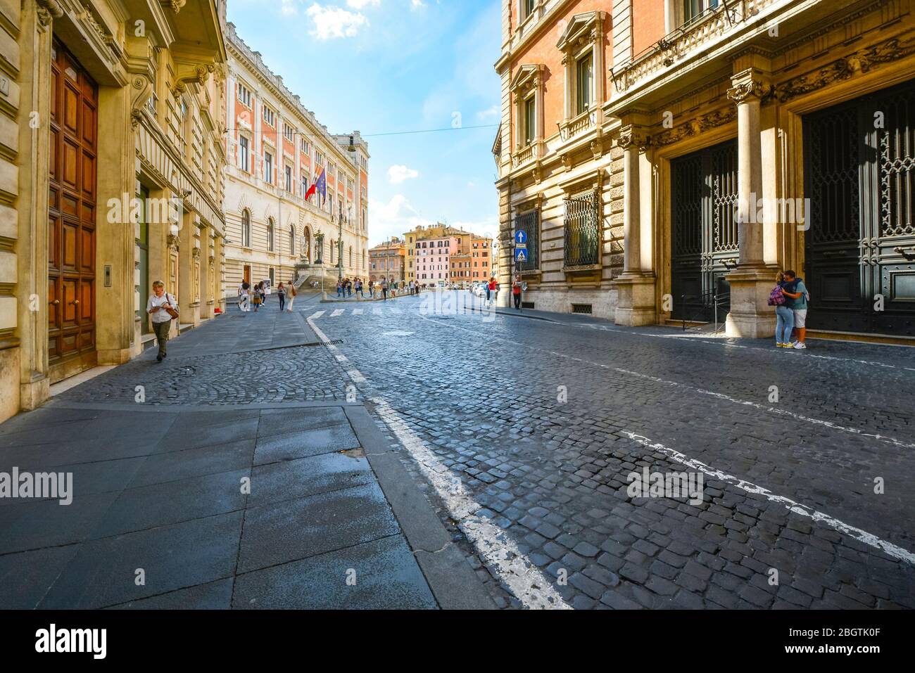 Un paio di abbracci sul marciapiede mentre i turisti e la gente del posto camminano lungo un'ampia strada vuota vicino a Piazza Navona a Roma Foto Stock
