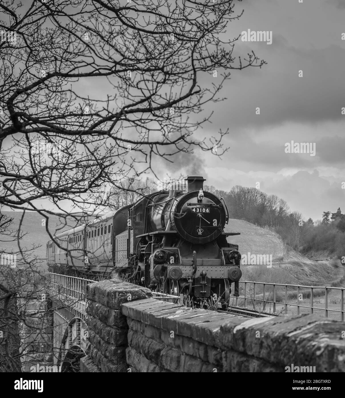 Vista frontale monocromatica del treno a vapore britannico d'epoca che si avvicina nella campagna rurale del Worcestershire, attraversando il ponte, Severn Valley Railway, Regno Unito. Foto Stock