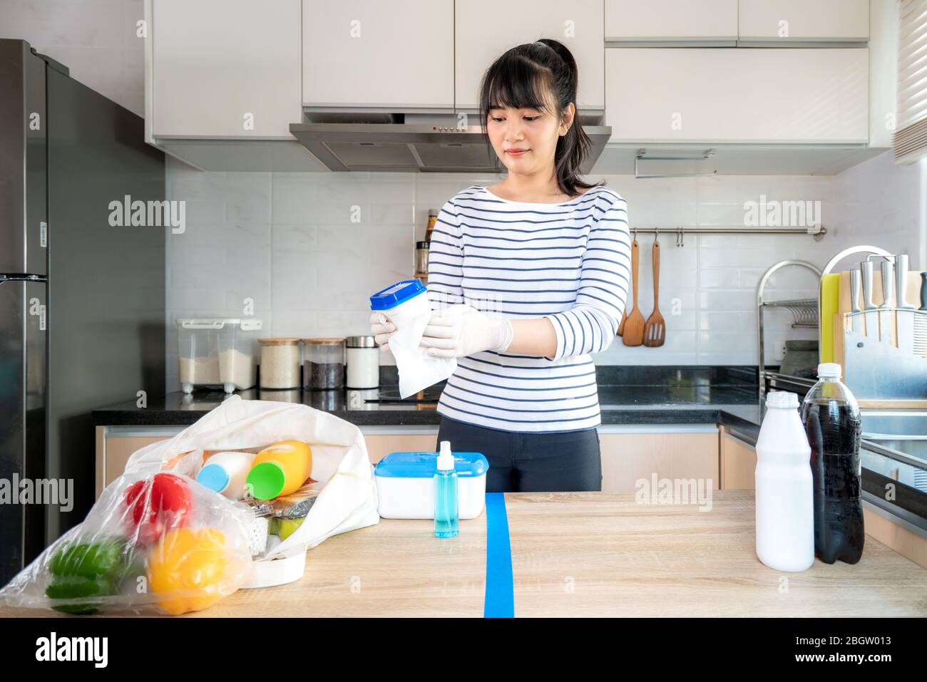 Giovane donna asiatica che stendono i generi alimentari su un tavolo diviso e strofinando giù yogurt o contenitori di latte bottiglia con disinfettante prendere per eliminare la cha Foto Stock