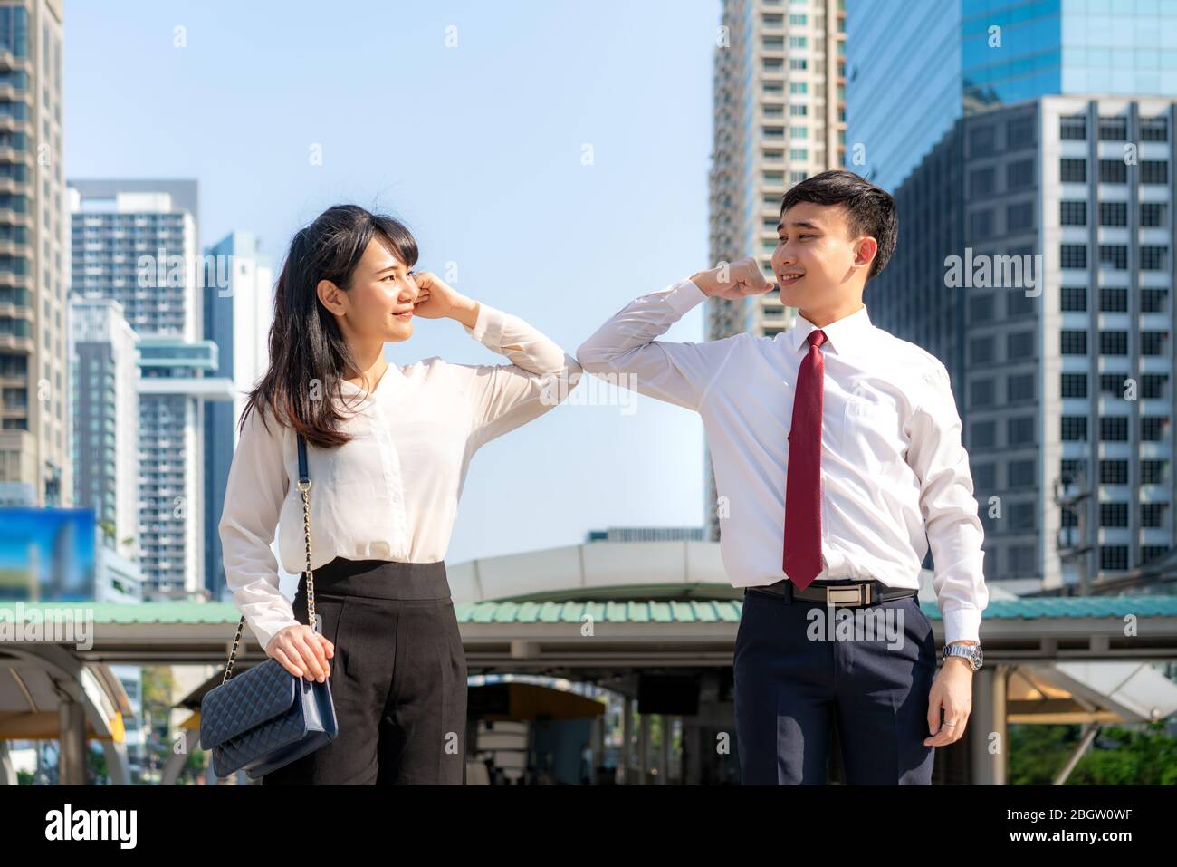 Gomito bump è nuovo saluto per evitare la diffusione di coronavirus. Due amici d'affari asiatici si incontrano di fronte all'edificio degli uffici. Invece di salutare Foto Stock