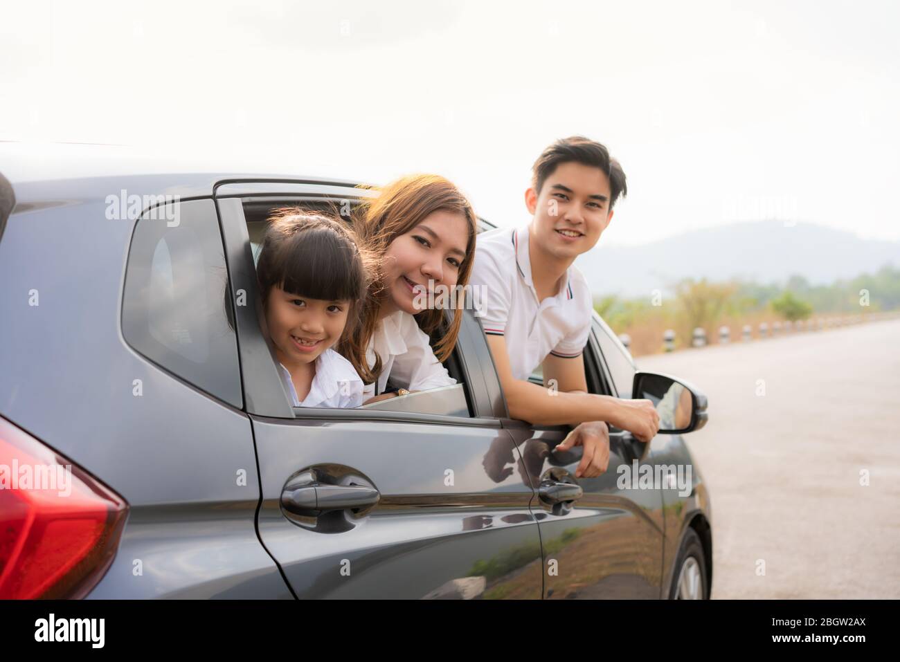 Felice famiglia asiatica con padre, madre e figlia in auto compatta sono sorridenti e guidare per viaggiare in vacanza. Assicurazione auto o noleggio e famiglia Foto Stock