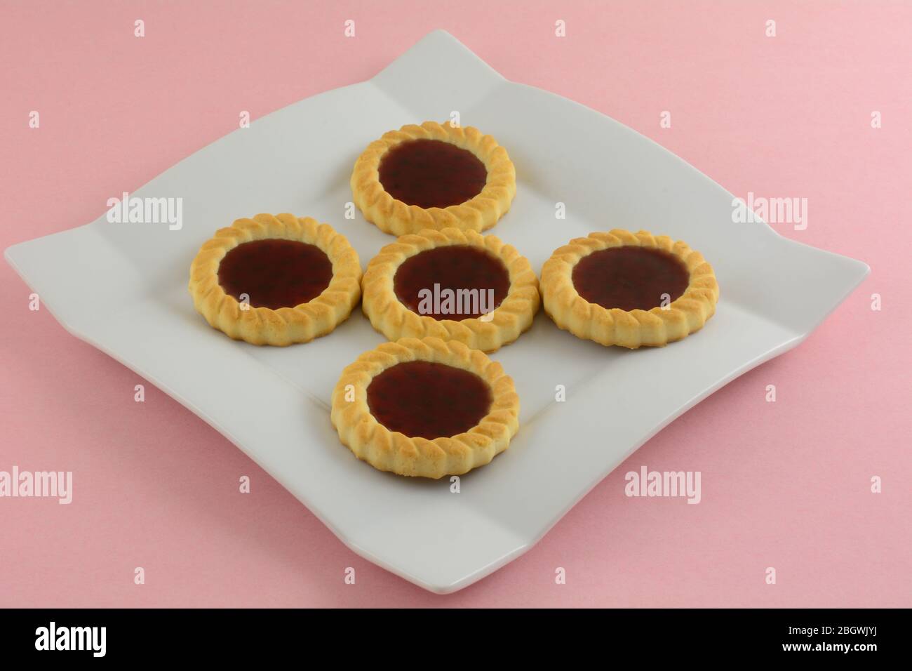 Primo piano di biscotti tartlette di frutta di lamponi rossi su piatto da dessert bianco su sfondo rosa Foto Stock