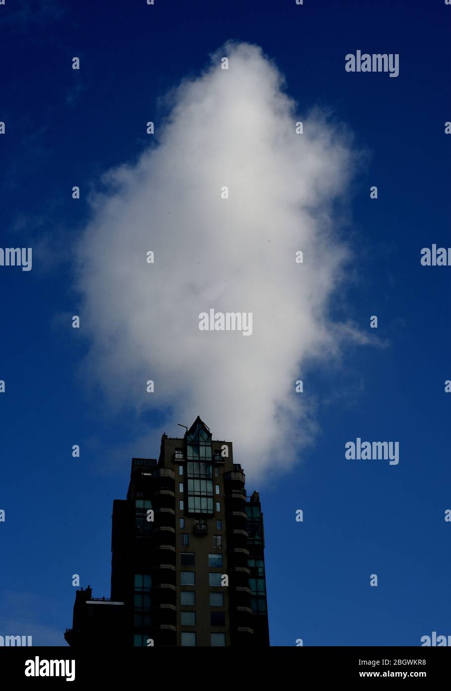 Una nuvola bianca verticale si trova in un cielo blu scuro sopra un moderno edificio in stile condominio di appartamenti nel West End di Vancouver, British Columbia, Canada. Foto Stock