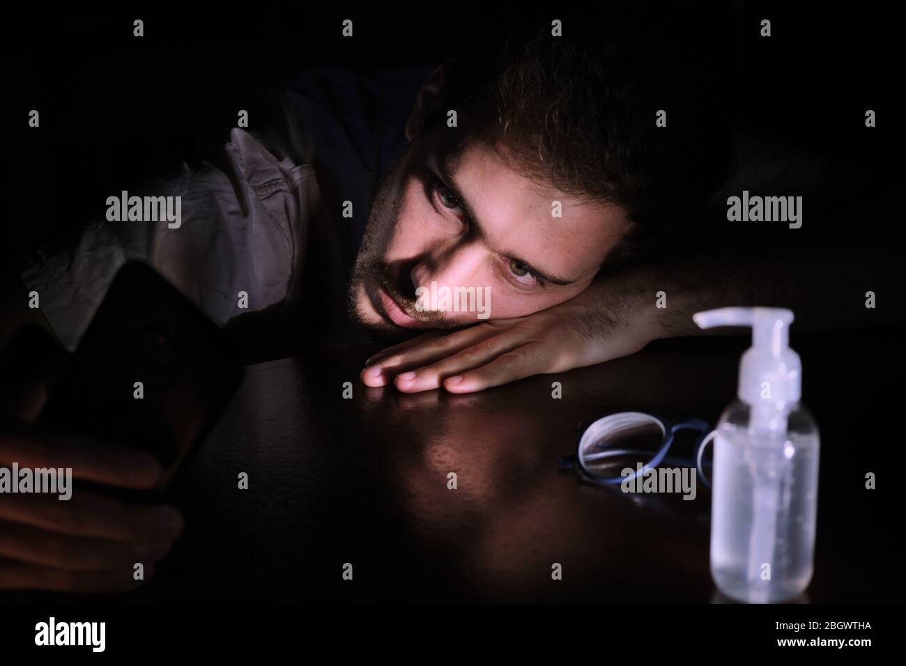 un medico si è sfinito di riposare sul tavolo di notte con lo schermo del cellulare illuminazione, il chinstrap e l'alcool gel durante la covid 19 pandemia Foto Stock