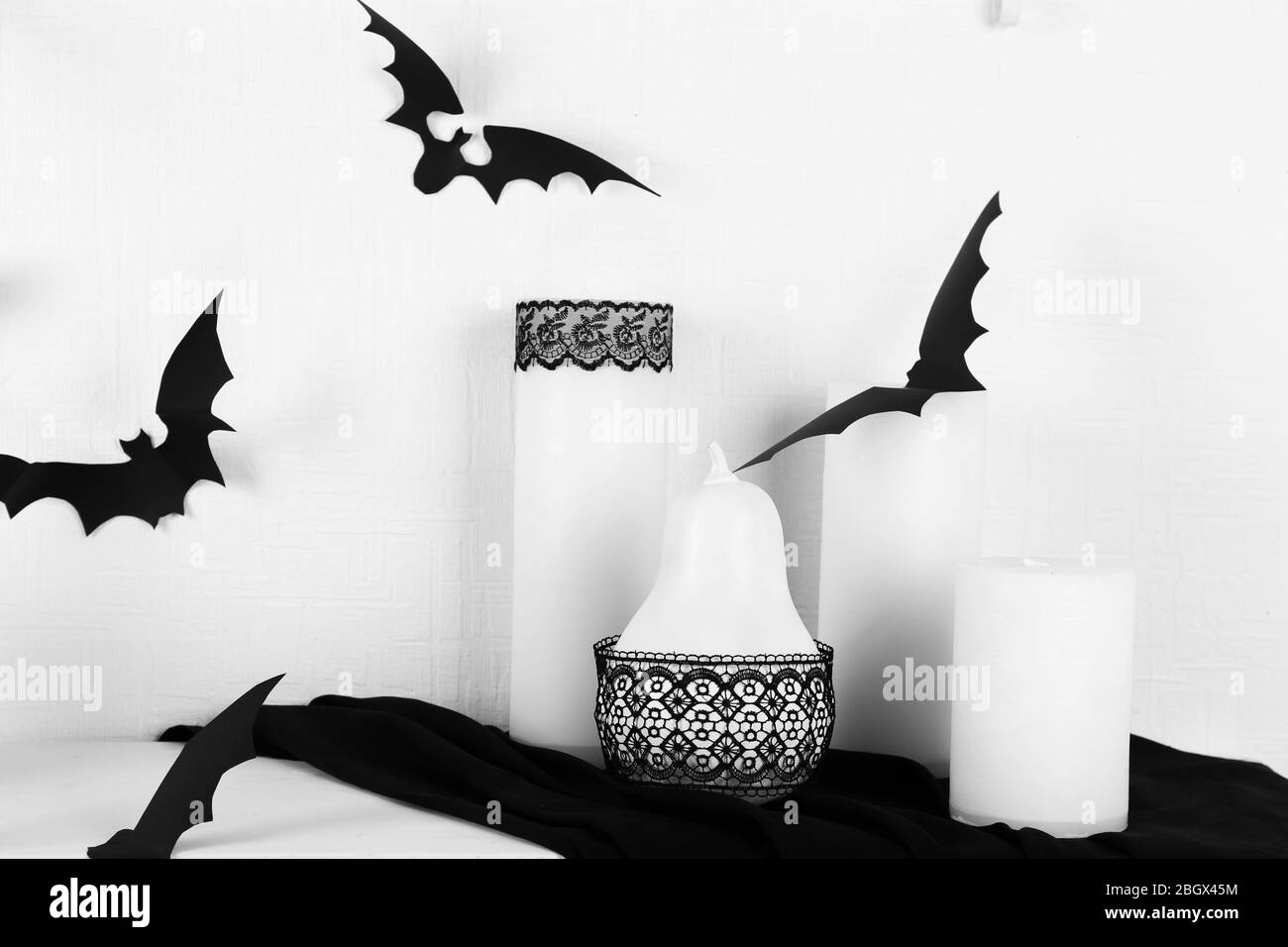 Le candele e i pipistrelli di carta sulla tavola sul muro bianco sullo sfondo Foto Stock