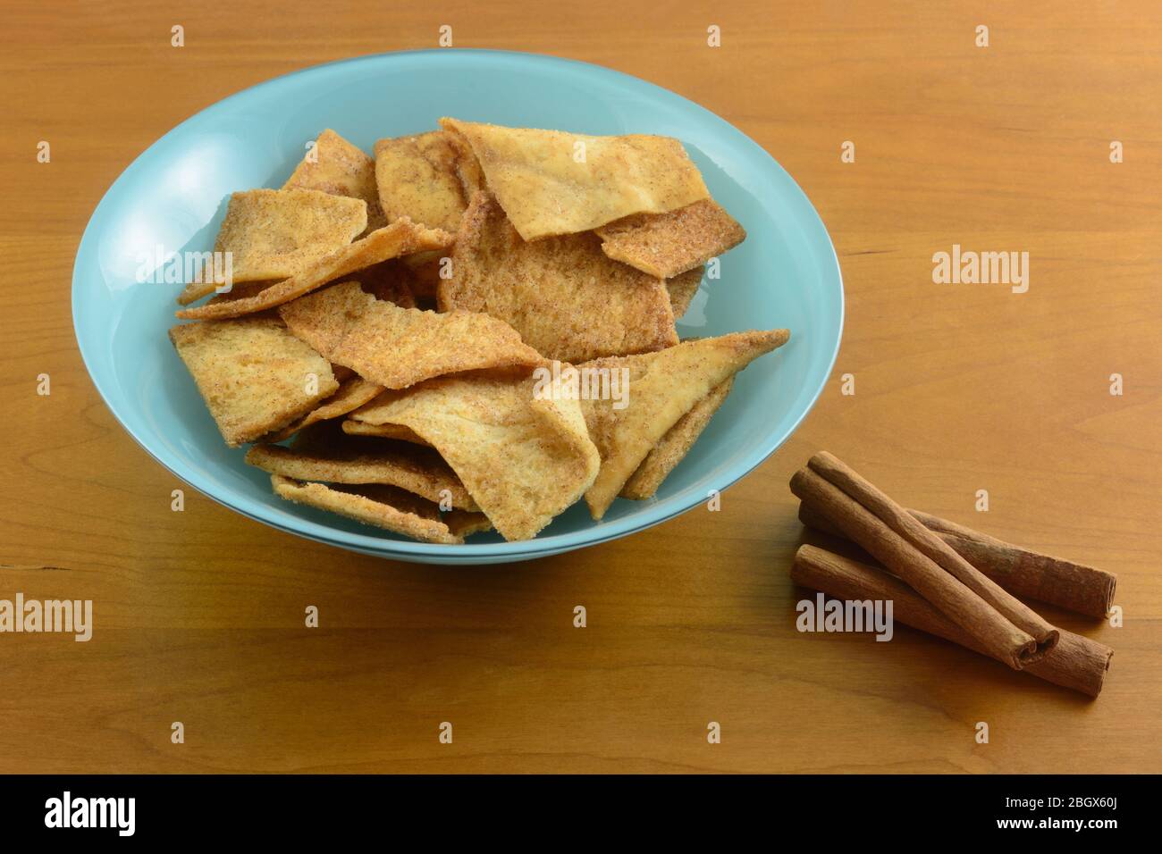 Patatine di pane pita di zucchero di cannella in ciotola blu con bastoncini di cannella su sfondo di legno Foto Stock