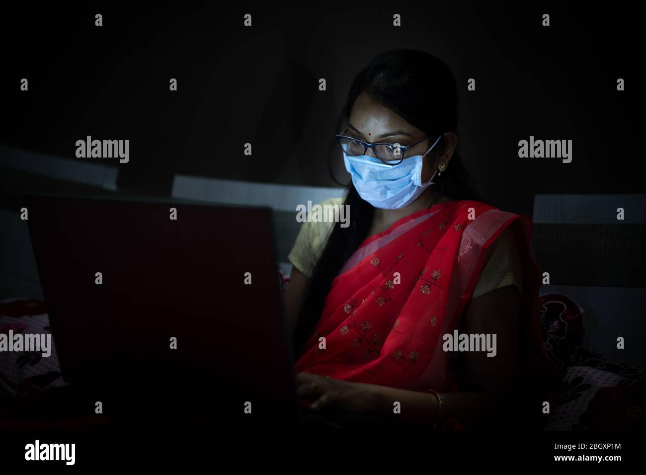 Giovane donna indiana che indossa la maschera di lavoro sul suo notebook a tarda notte, freelancer che lavora da casa. Coronavirus, Covid-19. Soggiorno a casa stare al sicuro, donna in qu Foto Stock