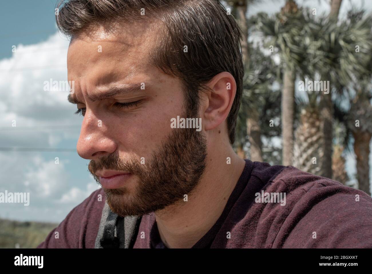 Un uomo che indossa una camicia rossa si siede a sentire giù nella vita mentre si affolce nel suo dolore luminoso giorno di sole su una panchina del parco Foto Stock