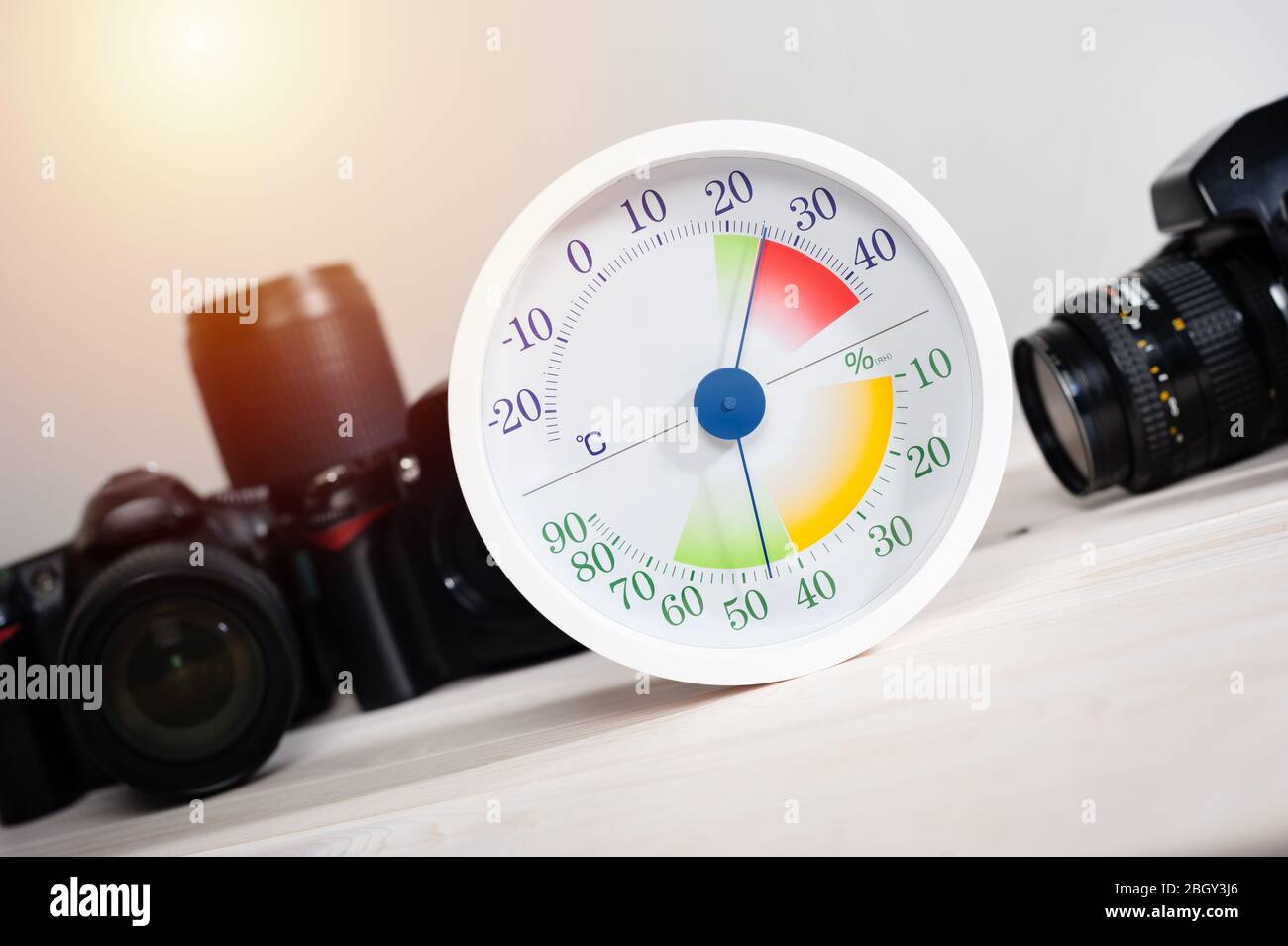 Termometro analogico bianco e igrometro con attrezzature fotografiche. Gli obiettivi e le apparecchiature della telecamera sono conservati in modo ottimale a un'umidità relativa (RH) di A. Foto Stock