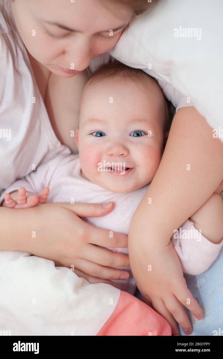 Mamma e figlia felici si trovano sulle spalle. Felice bambino sorridente sdraiato a casa sul letto. Bella ragazza sorridente con occhi blu. Vista dall'alto. Disposizione piatta. Foto Stock