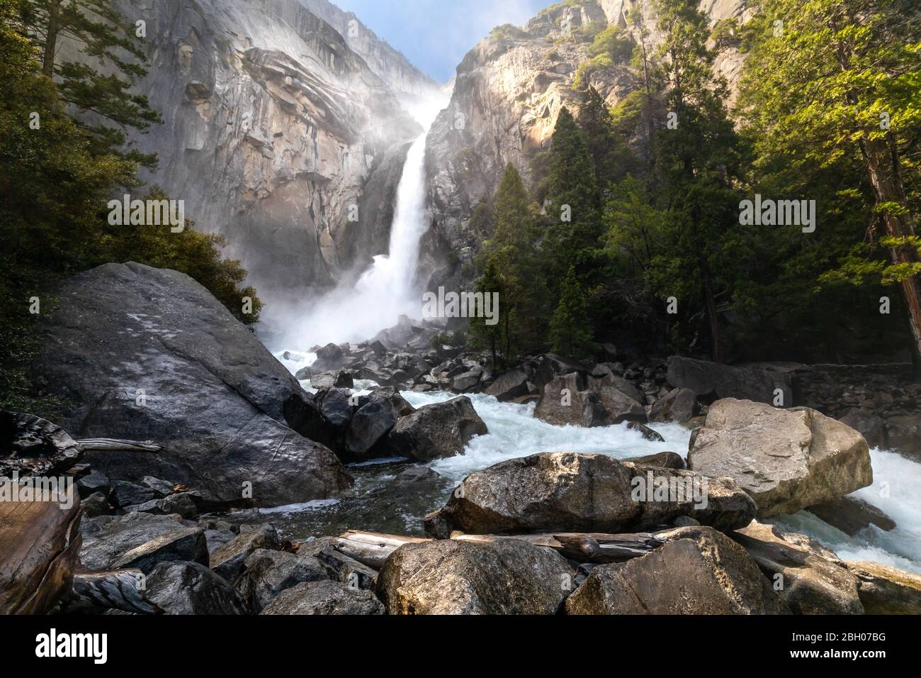 La cascata delle cascate inferiori di Yosemite, vista da Vista Point, con rocce in primo piano e alberi su entrambi i lati Foto Stock