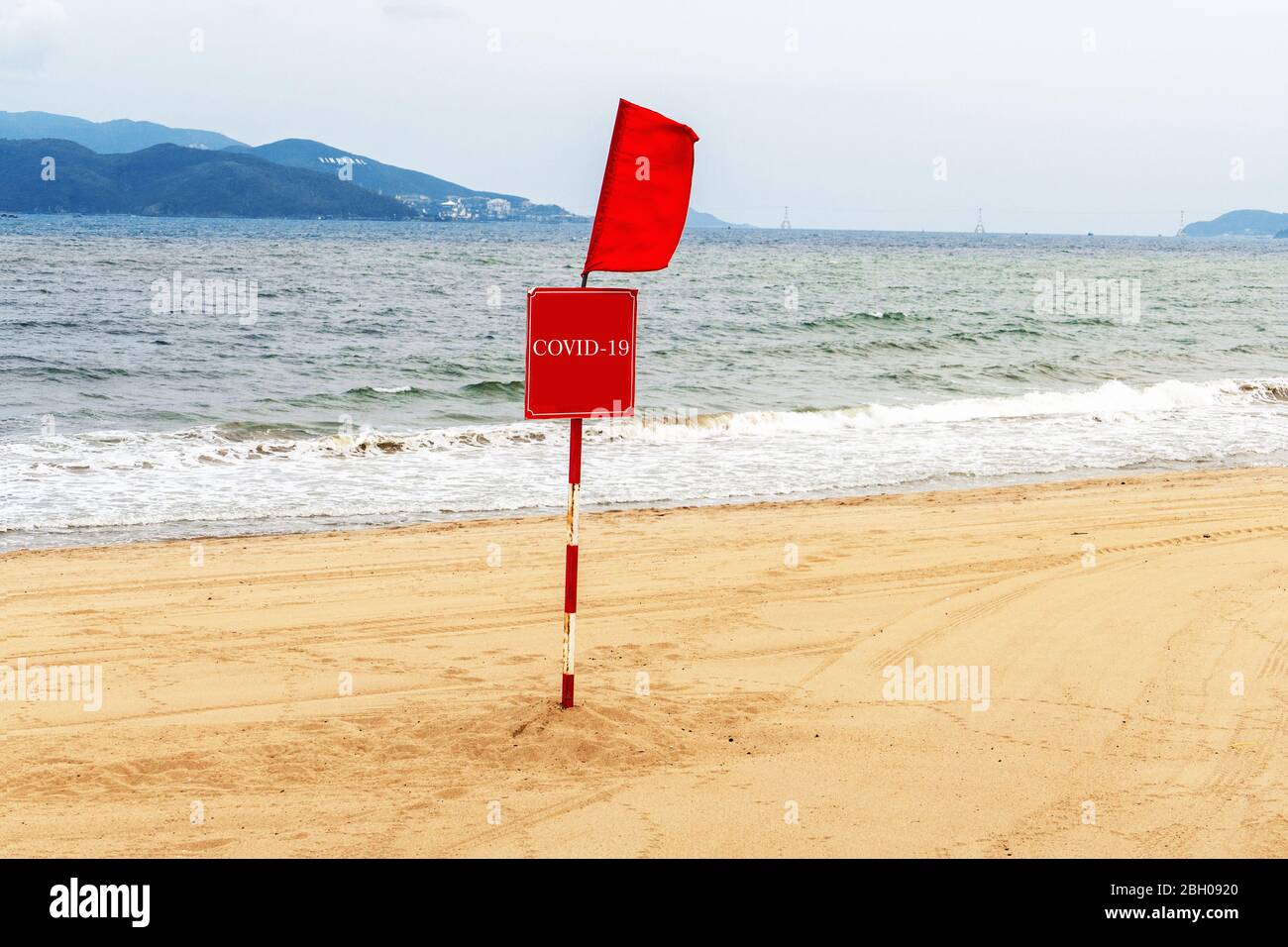 Сlosed spiaggia a causa delle misure di protezione contro la diffusione del virus COVID-19. Una bandiera rossa e un segnale di avvertimento che è vietato rimanere e nuotare su t Foto Stock