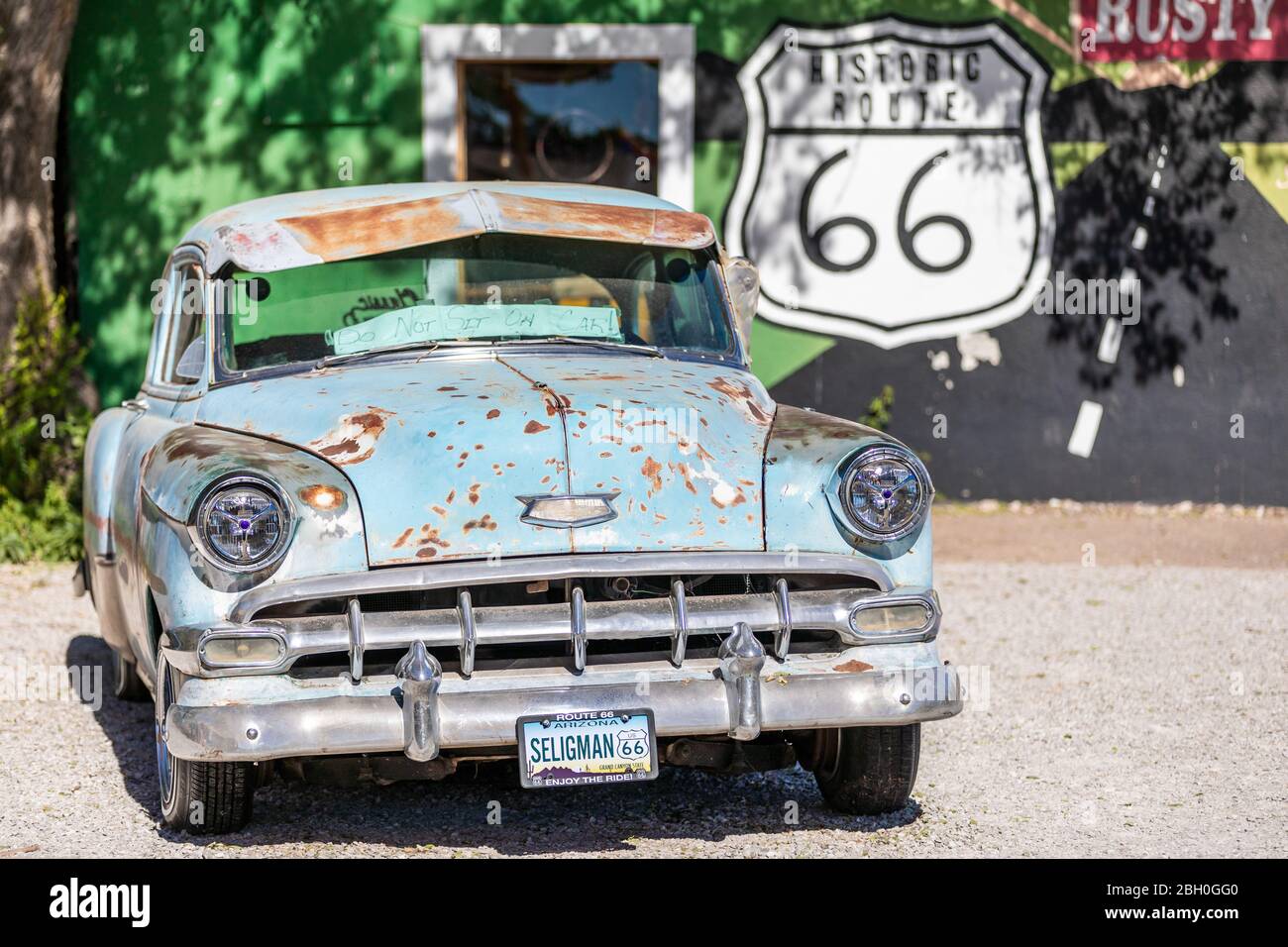 Primo piano di una vettura d'epoca arrugginita di colore azzurro parcheggiata, di fronte a un graffito della Route 66 Foto Stock