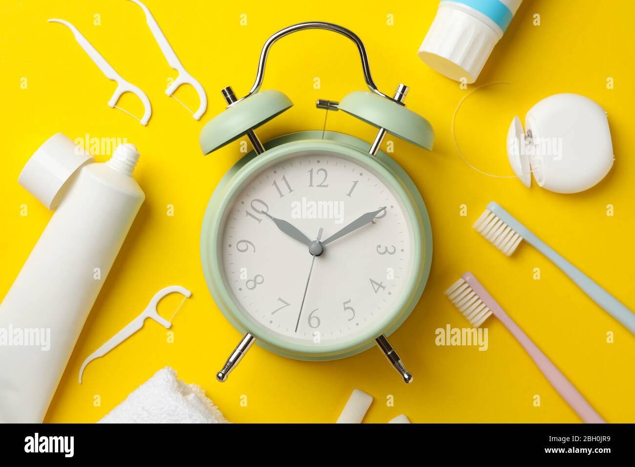 Sveglia e strumenti per la cura dentale su sfondo giallo, vista dall'alto Foto Stock