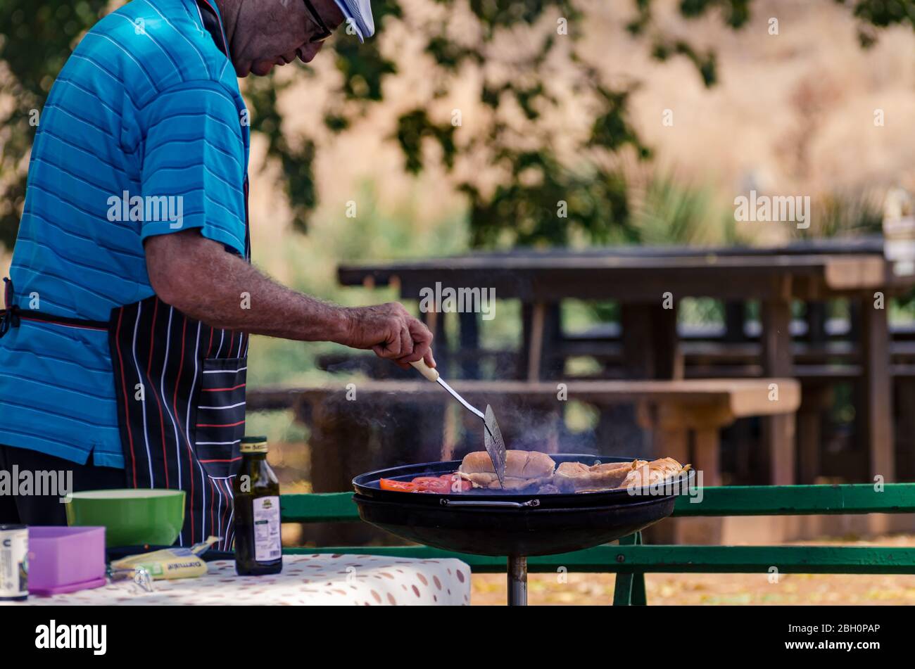 Uomo caucasico anziano grigliando carne all'aperto su un barbecue o braai in un'area picnic del parco safari nazionale Kruger Sud Africa Foto Stock