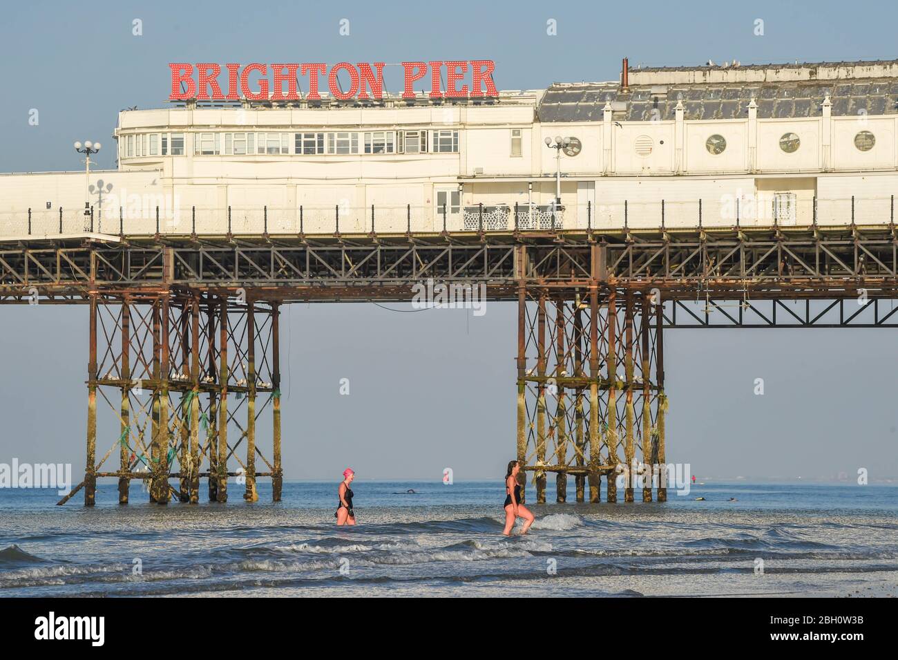 Brighton UK 23 Aprile 2020 - i nuotatori di prima mattina si godono un tuffo nel mare dal Brighton Palace Pier in una bella calda giornata di sole durante le restrizioni di blocco durante la crisi pandemica Coronavirus COVID-19 . Oggi le temperature dovrebbero raggiungere i 25 gradi in alcune parti del Sud Est . Credit: Simon Dack / Alamy Live News Foto Stock