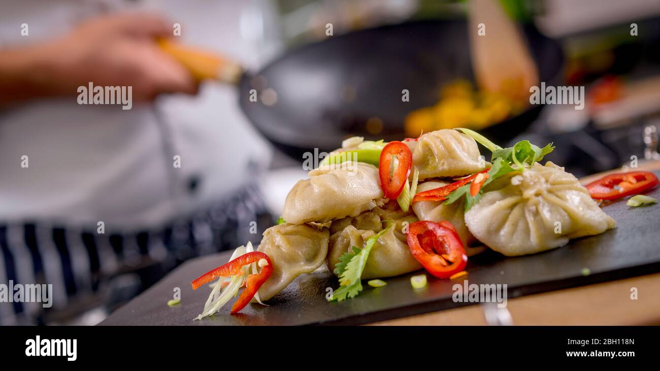 Uno chef prepara piatti nepalesi in cucina. Gnocchi Momo in guarnimento. Foto Stock