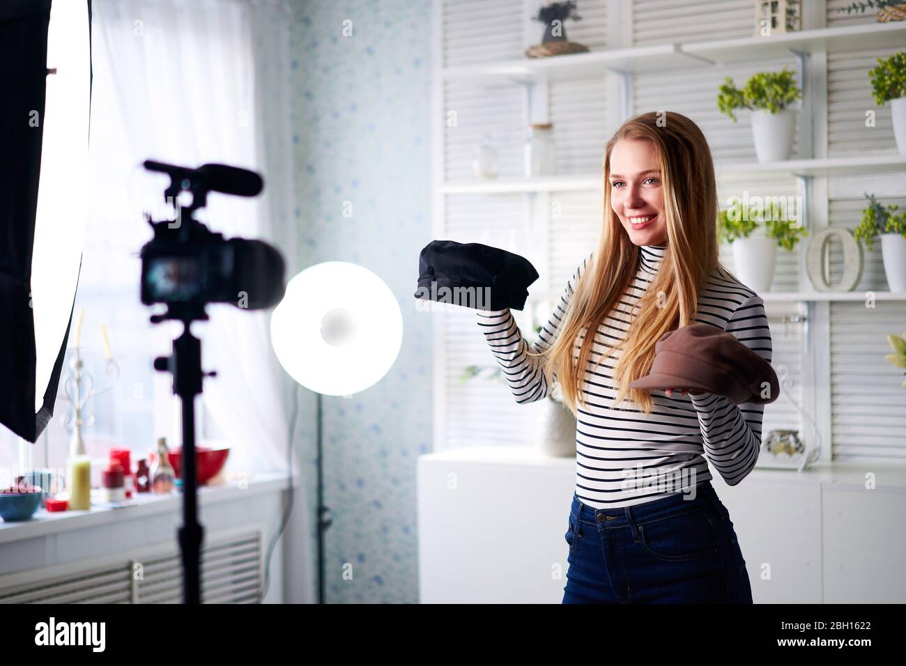 Donna blogger di moda in jeans e dolcevita mostrando i cappucci alla moda sulla fotocamera. Ragazza influencer stilista che mostra cappelli trendy filmare l'episodio vlog per Foto Stock