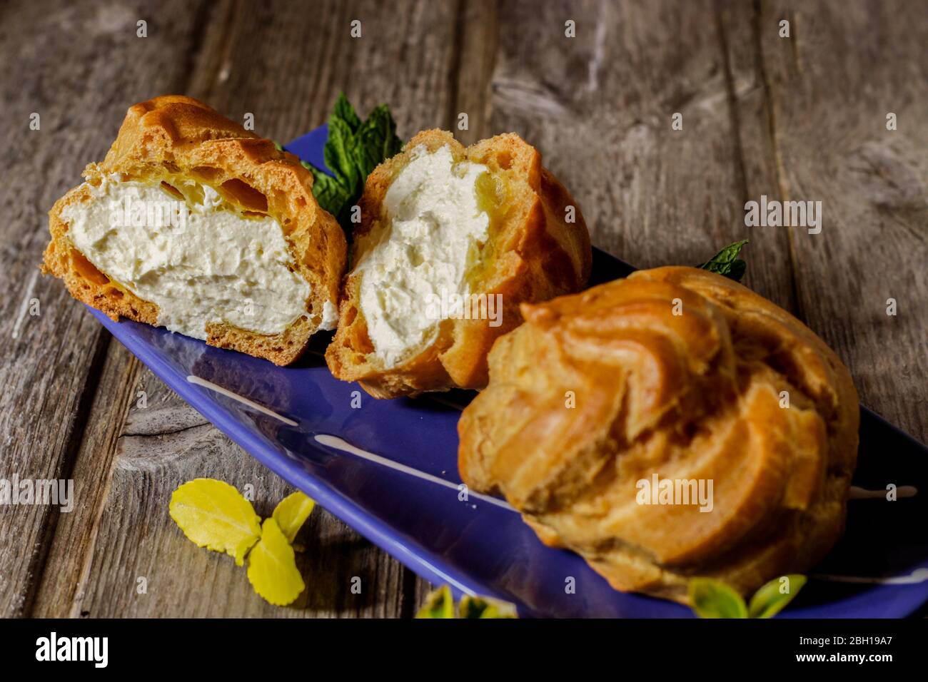 Deliziosi grandi purè di crema con crema in mano dipinto blu ovale piattino con foglie di menta su sfondo di legno invecchiato. Messa a fuoco selettiva. Foto Stock
