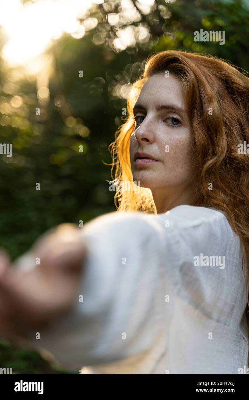 Giovane donna dai capelli rossi che le tira fuori le mani nella foresta Foto Stock