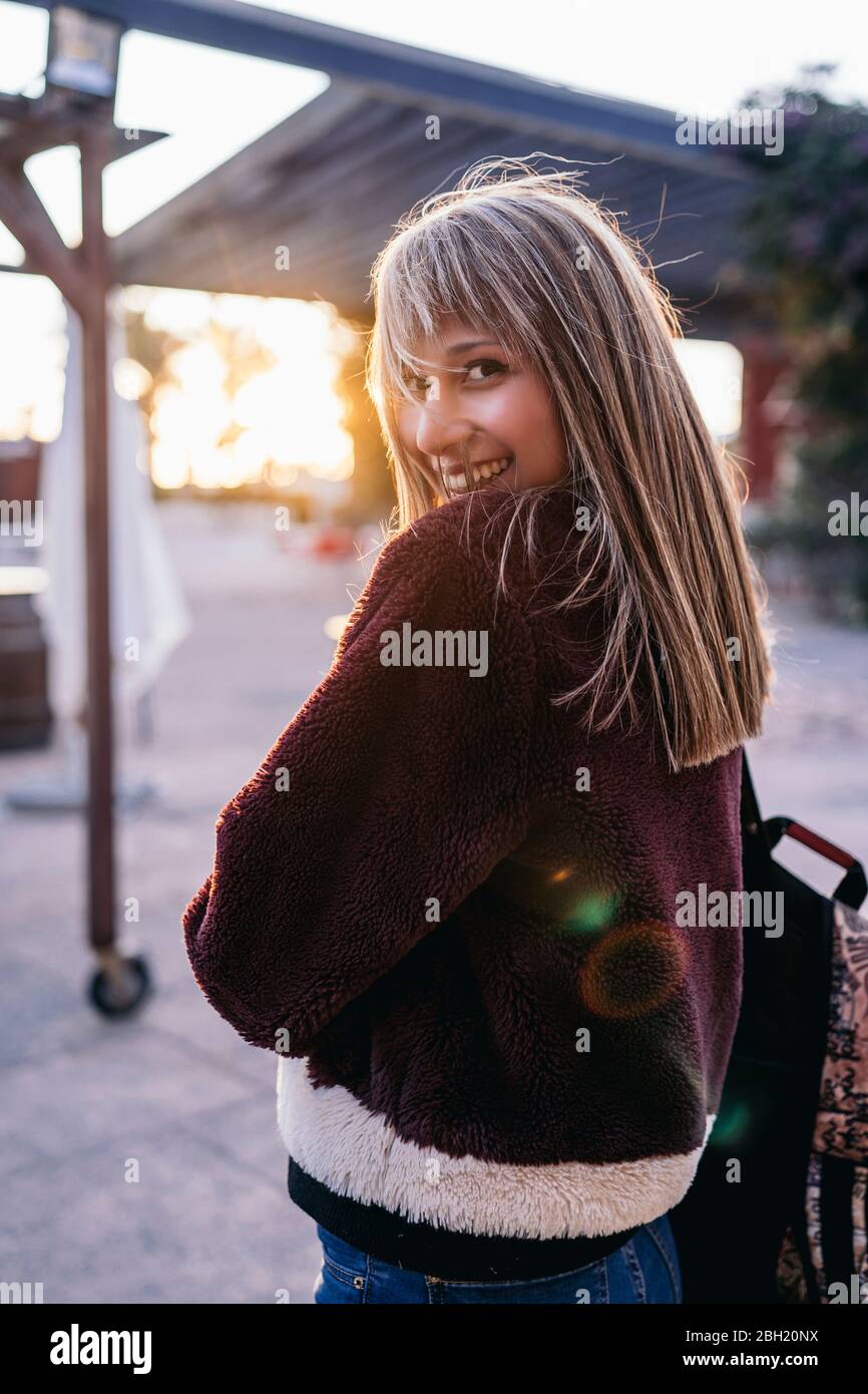 Giovane donna che indossa una giacca in pelliccia in città al tramonto Foto Stock