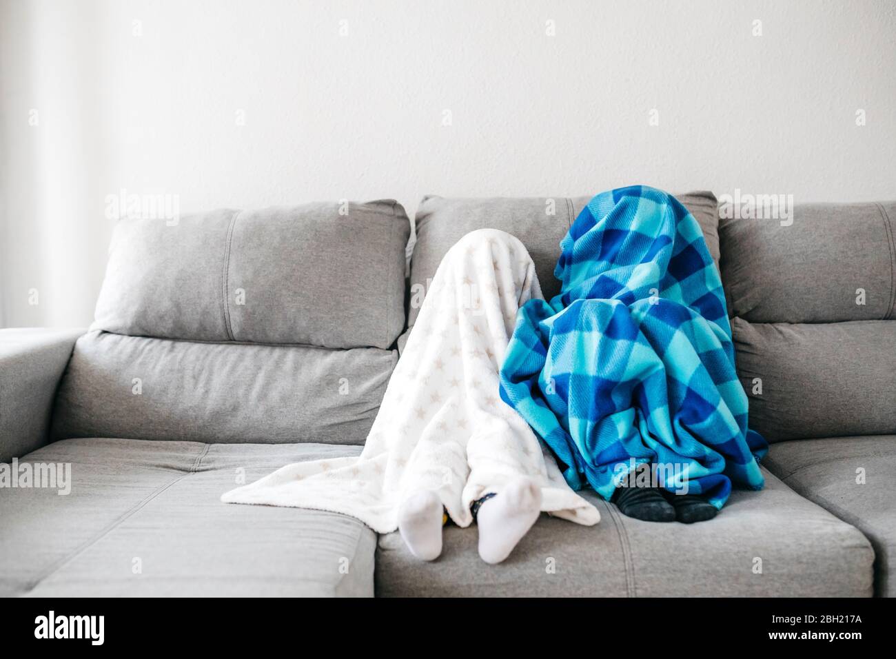Bambina e suo fratello seduti fianco a fianco sul divano a casa che si nasconde sotto le coperte Foto Stock