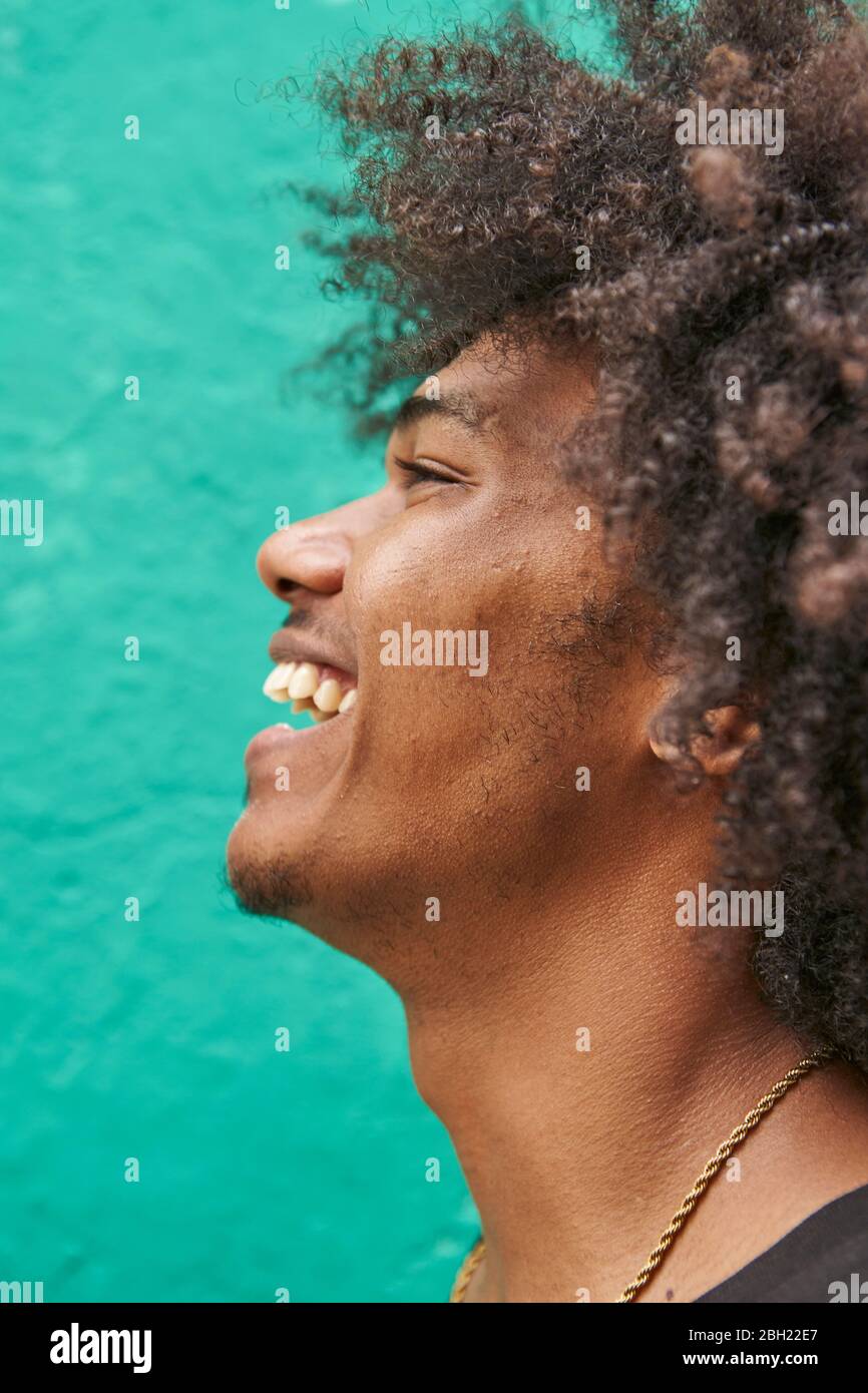 Profilo di ridere giovane con afro contro parete verde Foto Stock