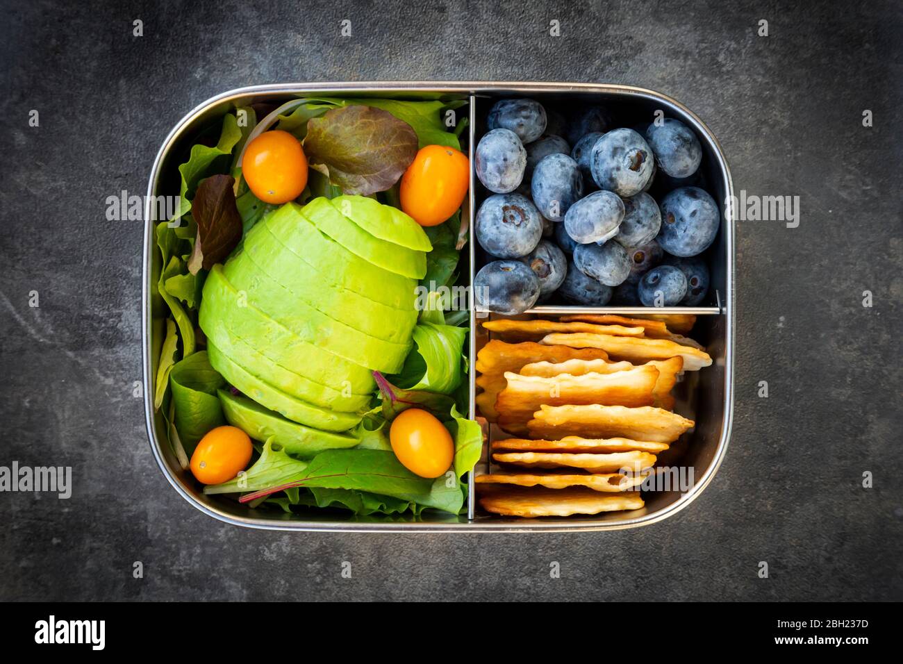 Pranzo al sacco con avocado a fette, pomodori gialli, cracker, mirtilli e insalata verde Foto Stock