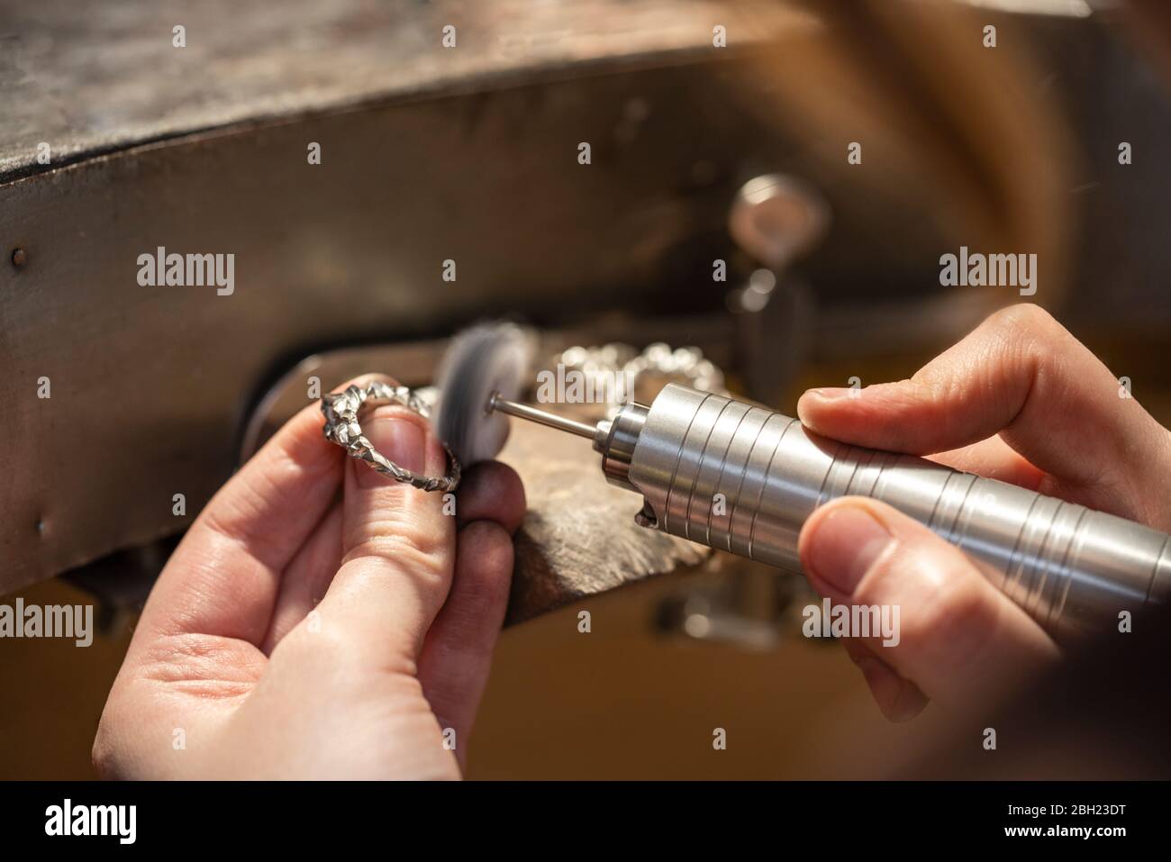 Mano di orafo femminile che lavora con smerigliatrice su anello d'argento Foto Stock
