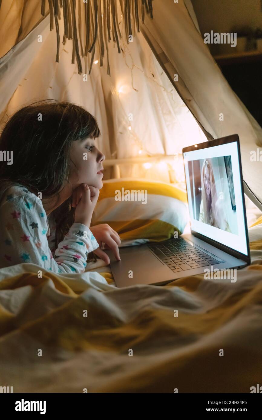 Ragazza sdraiata a letto di notte skyping con la madre che lavora fuori casa Foto Stock