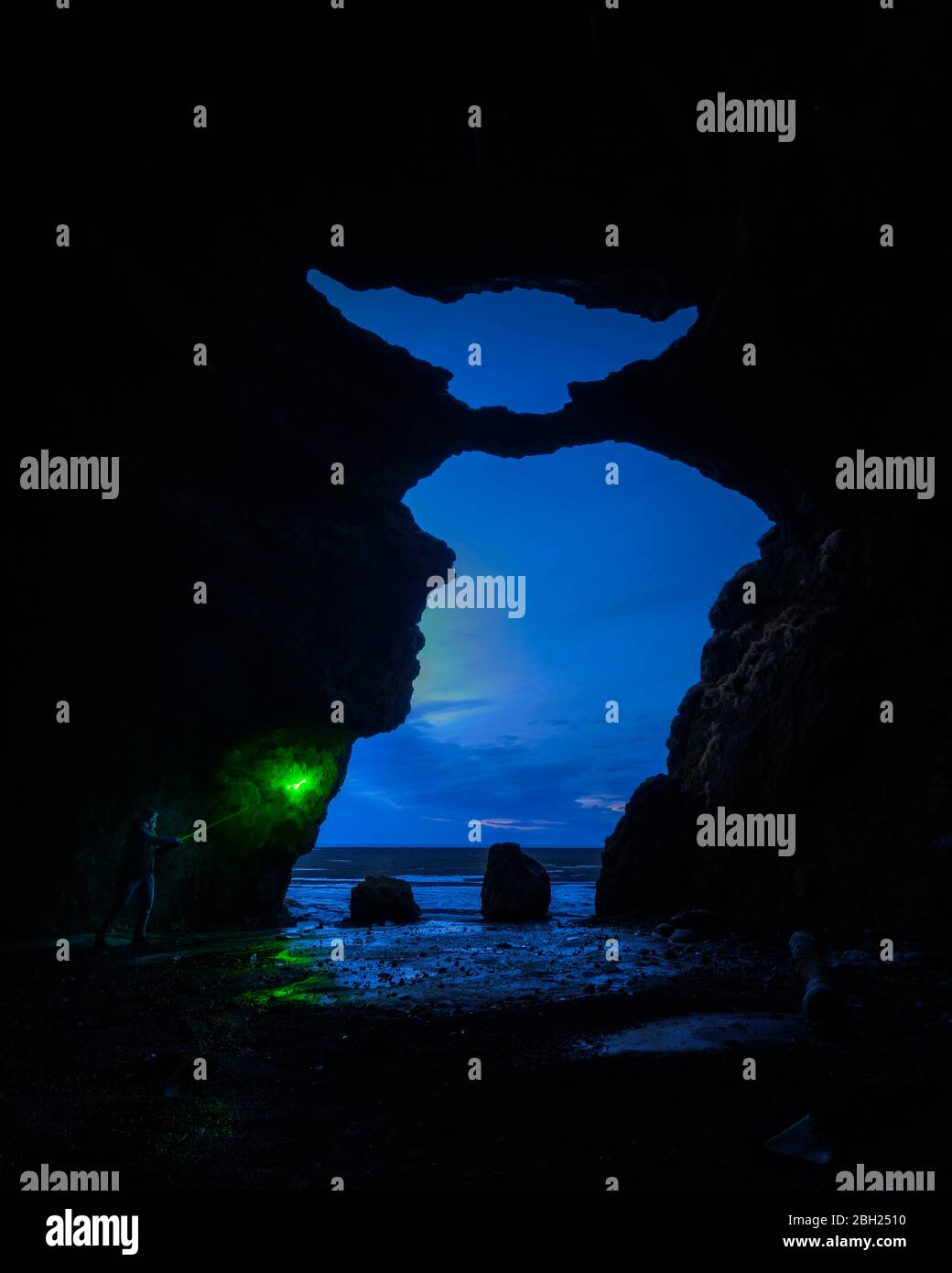 Islanda, Spelunker maschio che tiene il bastone di bagliore all'ingresso della Grotta di Yoda al tramonto Foto Stock