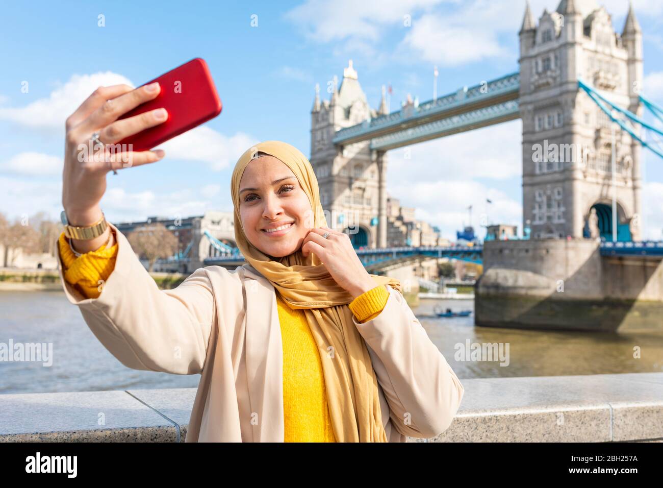 Ritratto di giovane donna sorridente che prende selfie con smartphone di fronte a Tower Bridge, Londra, Regno Unito Foto Stock
