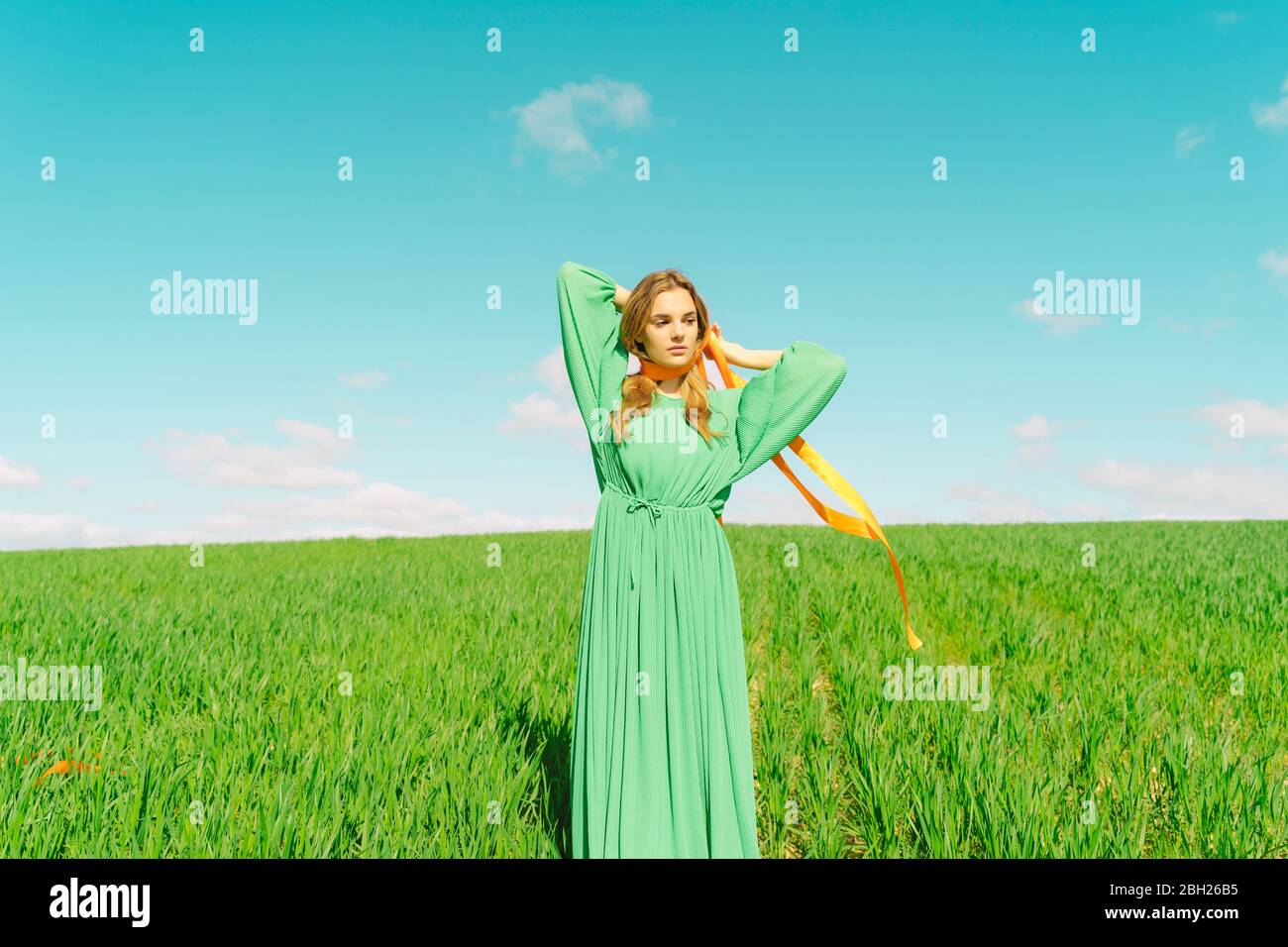 Giovane donna che indossa un vestito verde in piedi in un campo con un nastro intorno al collo Foto Stock