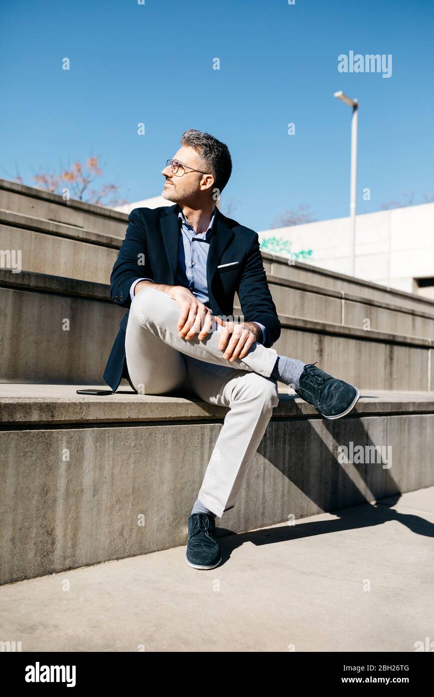 Uomo d'affari dai capelli grigi seduto sulle scale all'aperto Foto Stock