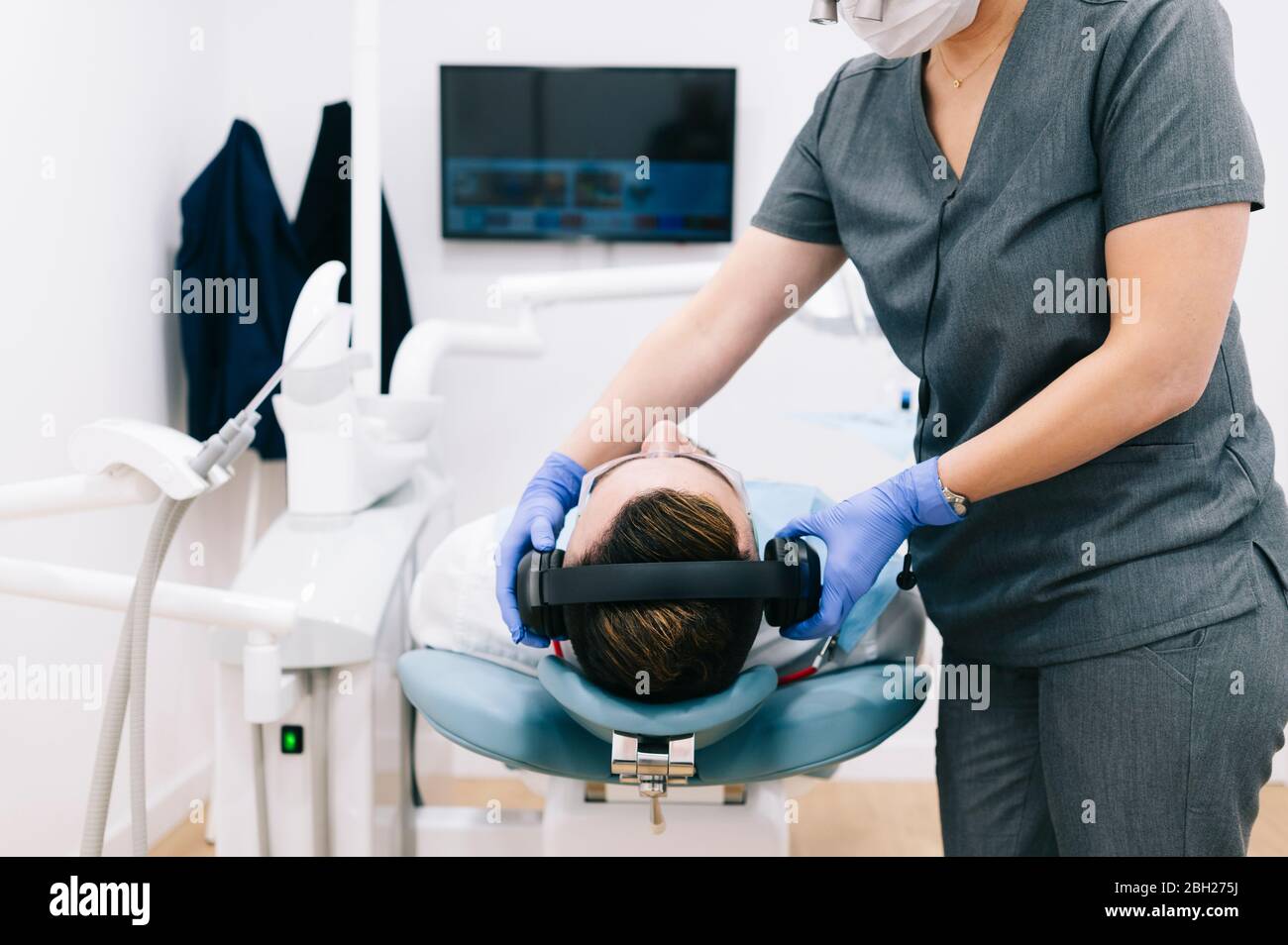 Dentista che indossa le cuffie sulla testa del paziente Foto Stock