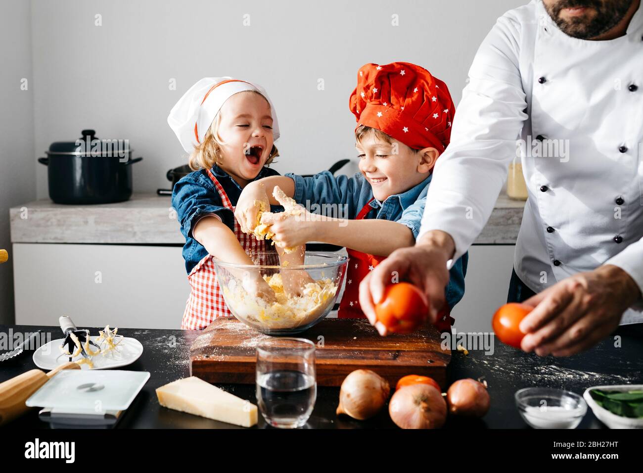 Felici i bambini che preparano l'impasto con il padre in cucina a casa Foto Stock