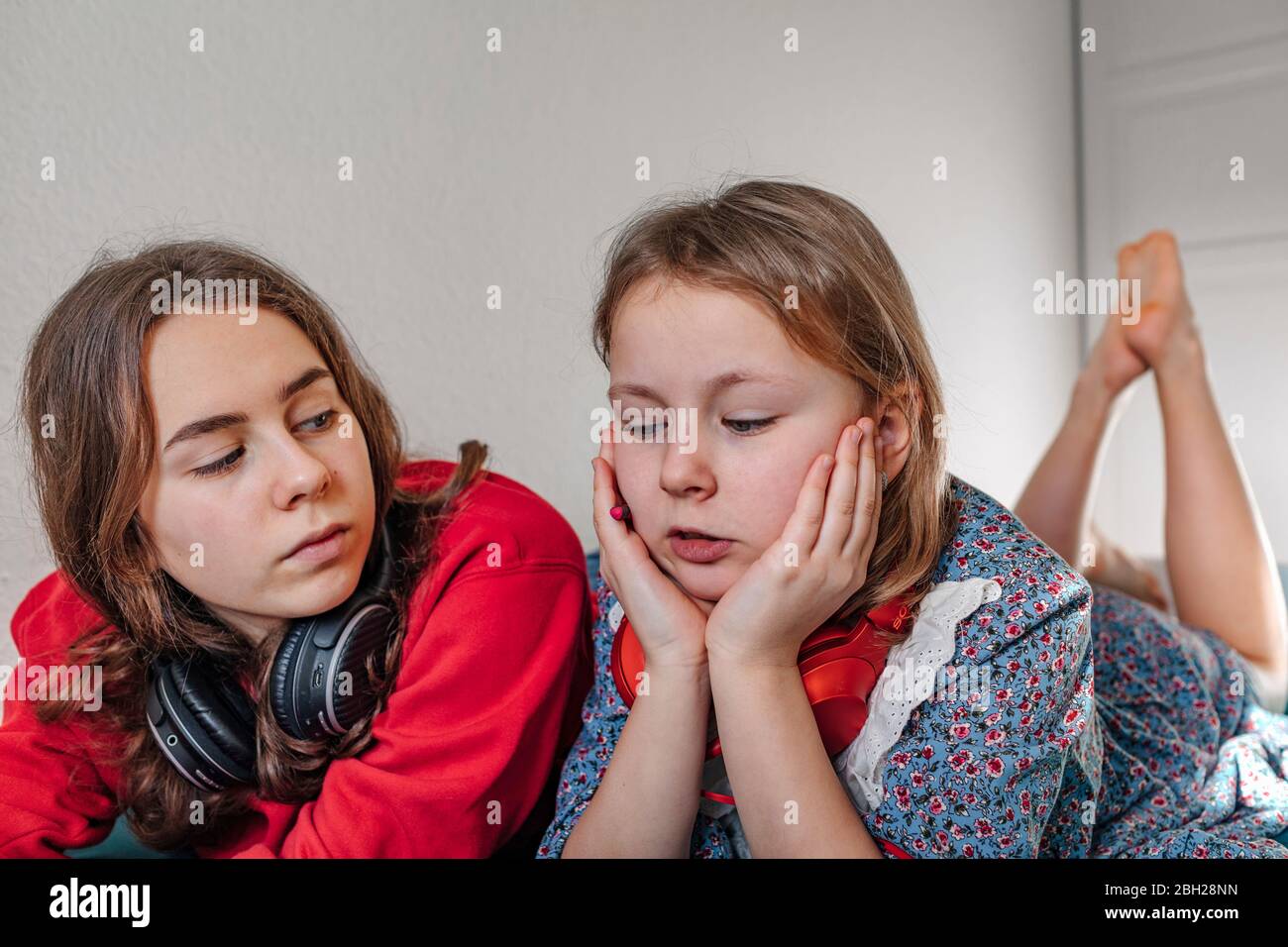 Ritratto di due sorelle con cuffie che si stendono insieme sul letto Foto Stock