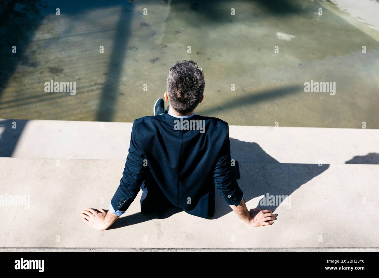 Vista posteriore e uomo d'affari con capelli grigi seduto sulle scale in una piscina Foto Stock