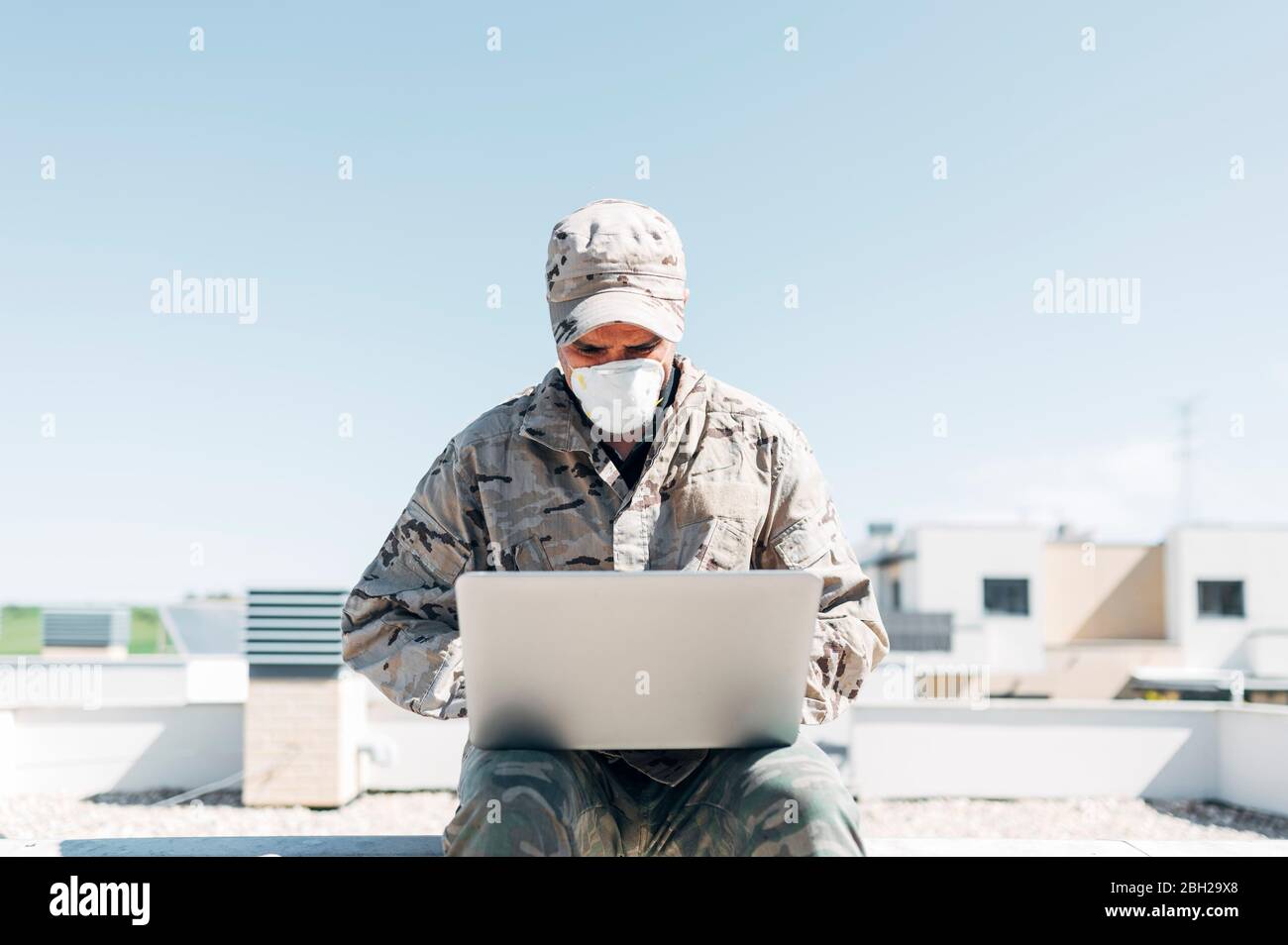 Soldato con maschera facciale in caso di emergenza, utilizzando un computer portatile Foto Stock