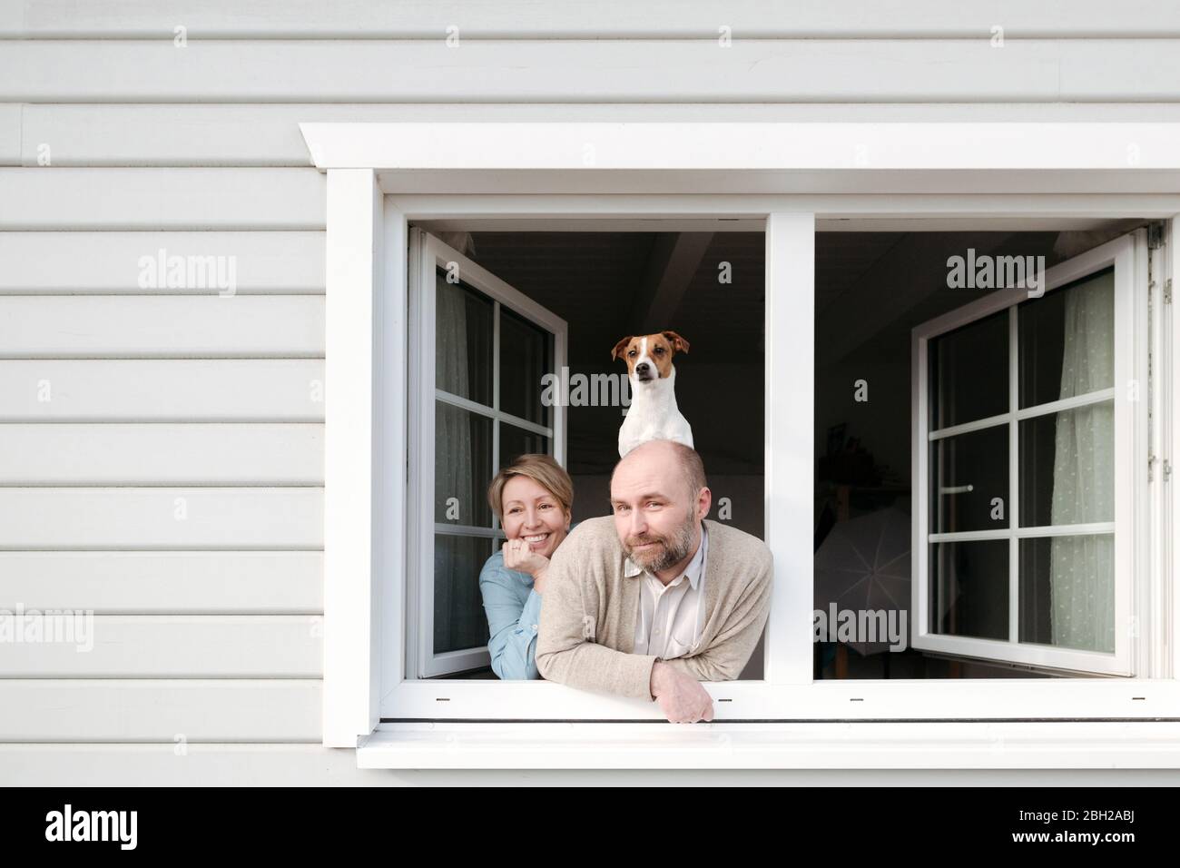 Coppia con il cane che si appoggia fuori dalla finestra della loro casa Foto Stock