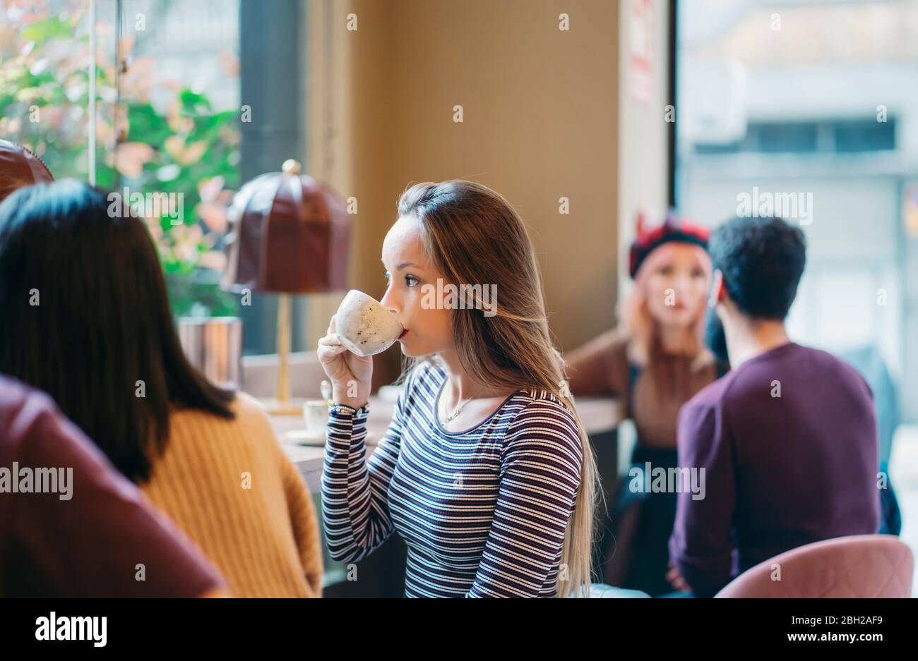 Giovane donna seduta nel bar occupato di un ristorante, bere caffè Foto Stock