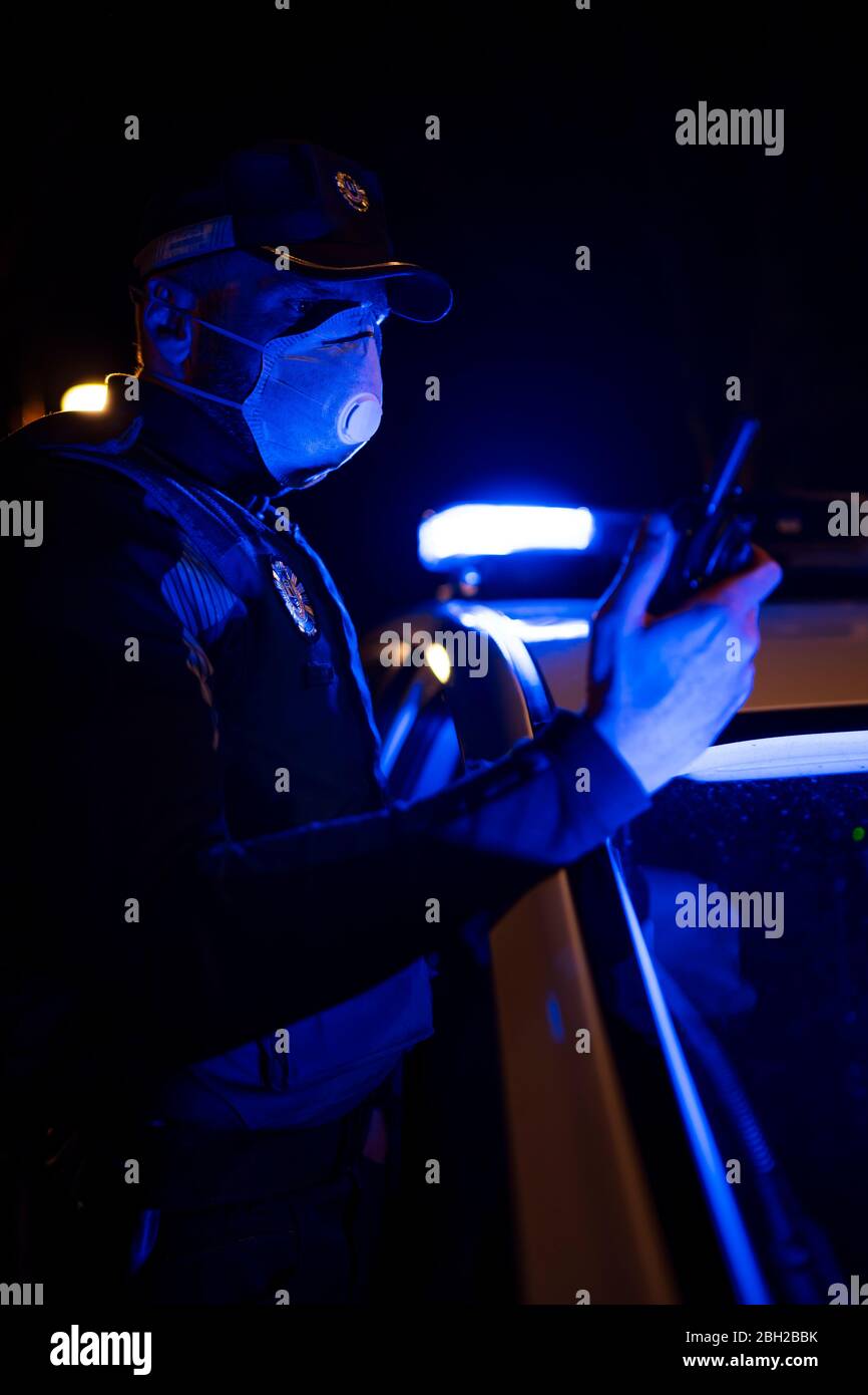 Poliziotto in missione di emergenza, indossare maschera facciale, tenere telefono Foto Stock