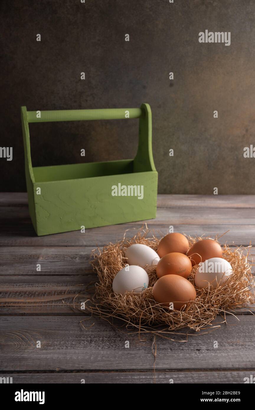 Uova di pollo marroni e bianche in un nido di paglia su sfondo di legno. Dietro una scatola di legno. Spazio sotto il testo Foto Stock