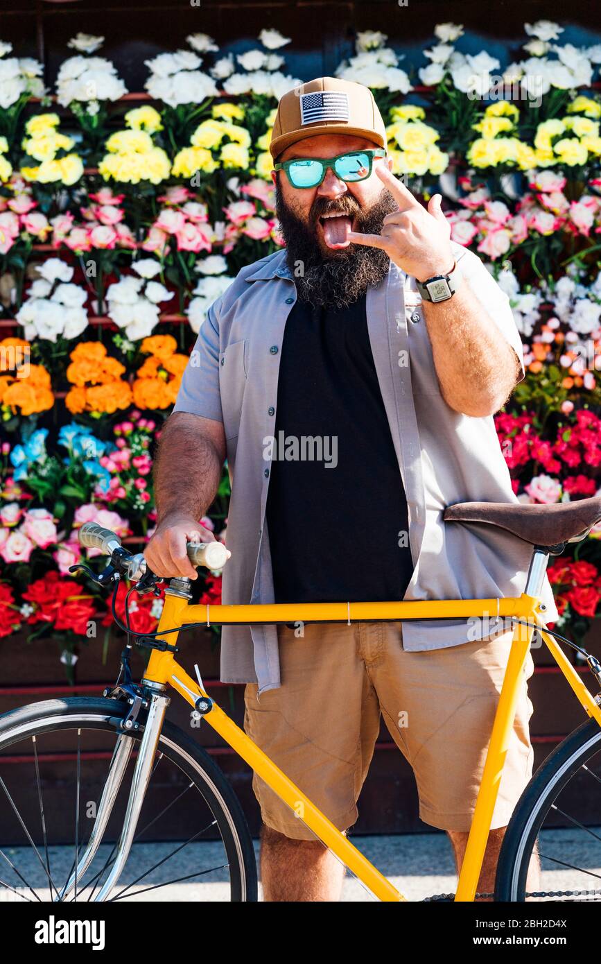 Ritratto di uomo con la bici fissa che si stacca dalla lingua e mostra il cartello Rock and Roll Foto Stock