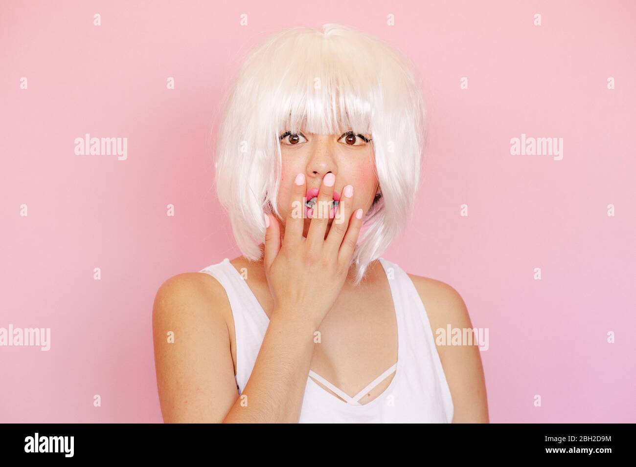 Ritratto di giovane donna spaventato con bocca di copertura a mano davanti a sfondo rosa Foto Stock