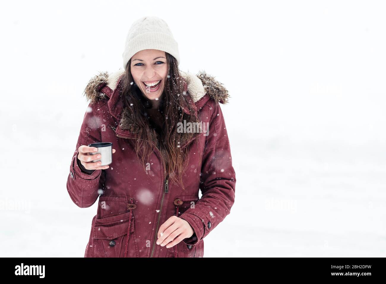 Ritratto di giovane donna ridente con bevanda calda nella neve Foto Stock